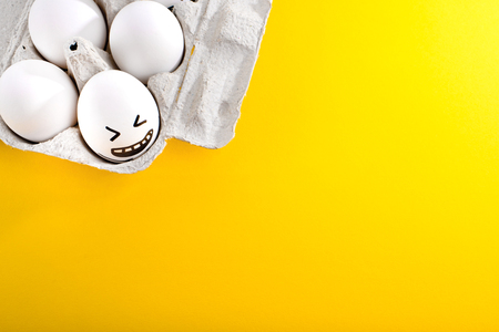 Easter eggs with drawn cartoon faces in tray on yellow background.の写真素材