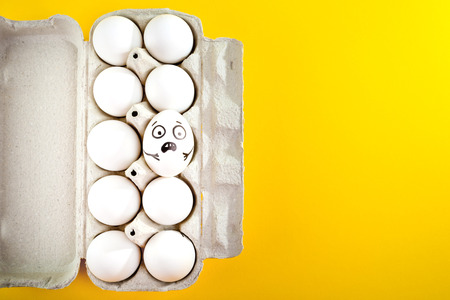 Easter egg with funny face in tray on yellow background.の写真素材