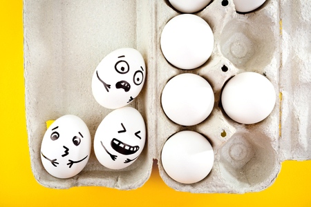 Easter eggs with drawn cartoon faces in tray on yellow background.の写真素材