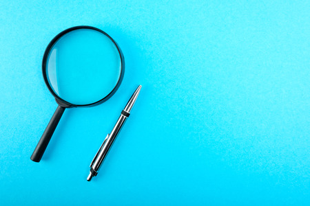 Magnifying glass and pen on blue table. Top view.の写真素材