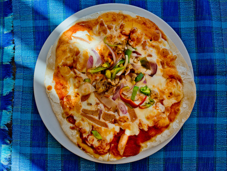 Pizza with bacon and green spicy pepper on a plate on a blue tablecloth. Top view.
