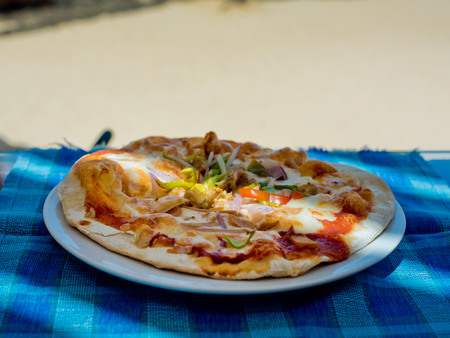 Pizza with bacon and green spicy pepper on a plate on a blue tablecloth in a cafe on the beach.の写真素材