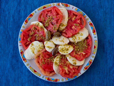 Delicious caprese salad with ripe tomatoes and mozzarella cheese on a round plate against a blue napkin. Top view.の写真素材
