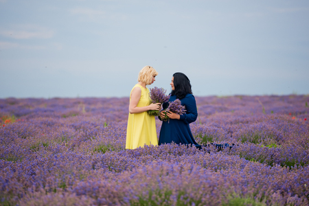 Two young girls with different hair color in blue and yellow dresses, posing together in a lavender field.の写真素材