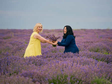 Two young girls with different hair color in blue and yellow dresses, posing together in a lavender field.の写真素材