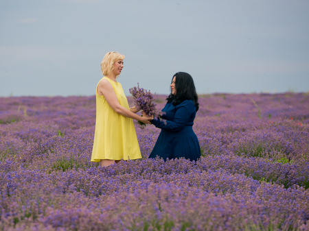 Two young girls with different hair color in blue and yellow dresses, posing together in a lavender field.の写真素材
