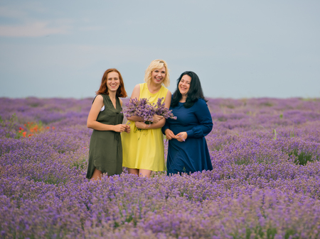 Three young girls with different hair color in different dresses, posing together in a lavender field.の写真素材