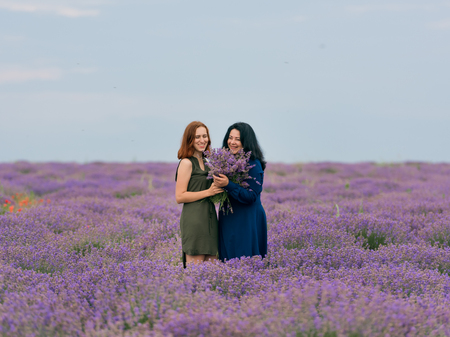 Two young girls with different hair color in blue and green dresses, posing together in a lavender field.の写真素材