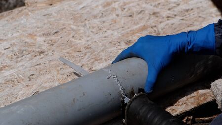 Plumber in rubber gloves, cuts the plastic sewer pipe, electric saber saw. Close-up.