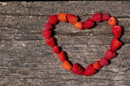 Heart made of ripe aromatic raspberrie on a wooden background.の写真素材
