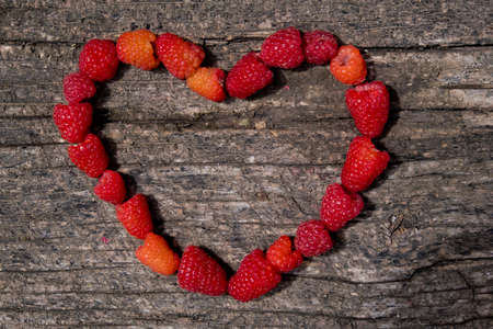 Heart made of ripe aromatic raspberrie on a wooden background.の写真素材