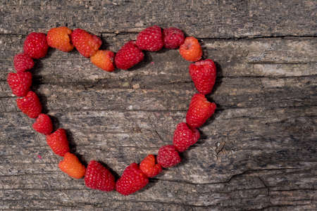 Heart made of ripe aromatic raspberrie on a wooden background.の写真素材