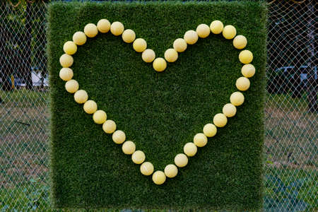 The shape of a heart on a green background is lined with tennis balls.の写真素材