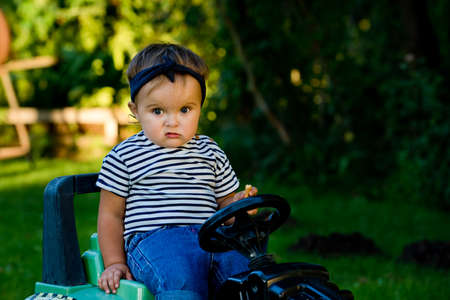 Baby girl playing with toy tractor in a garden. Closeup.