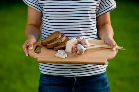Young woman holding wooden board with garlic, lard and bread. Closeup.の写真素材