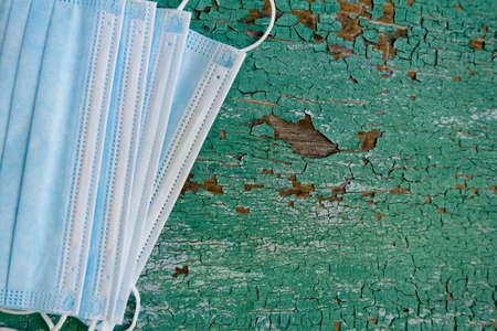 New medical disposable masks on background of green cracked paint on wooden planks.