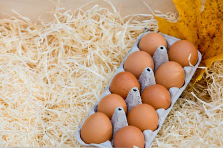 Tray of fresh chicken eggs in a wooden box against a background of autumn foliage. Close-up.