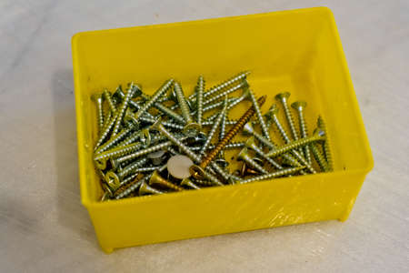 Close-up of small plastic yellow box with different screws and fasteners. Selective focus.