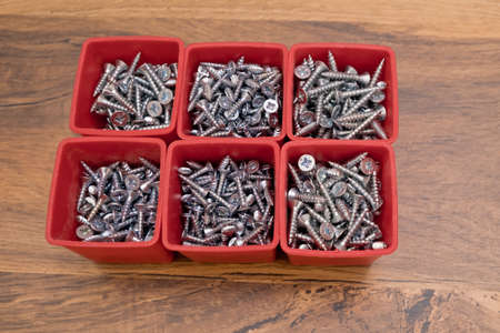 Various size and shape of screws selection in red plastic tray box on a wooden background.