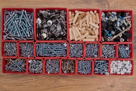 Various size and shape of screws, bolts, wooden pegs selection in red plastic tray box on a wooden background. Assembly kit for furniture. top view.の写真素材