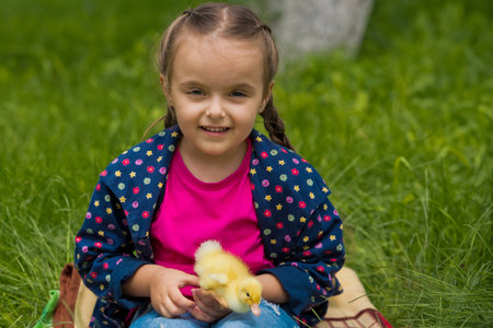 Cute happy little girl with small duckling in the garden. Little girl holding a duckling in her hands.の写真素材