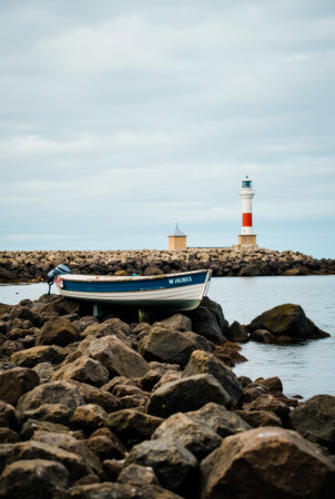 A small boat is beached on a rocky shore near a lighthouseの素材