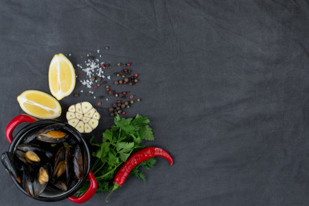 Casserole with mussels, lemons, chili pepper and spices on dark textile background. Flat lay.の写真素材
