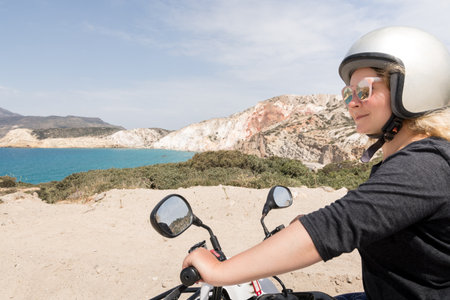 Young woman driving rental quad bike on seaside road in Milos island towards Firiplaka beach, Greeceの写真素材