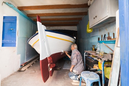 MANDRAKIA, GREECE - MAY 2018: Man Painting His Fishing Boat inside the Boathouse