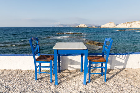 Table and chairs standing on the coast of Aegean sea in Greek island of Milosの写真素材