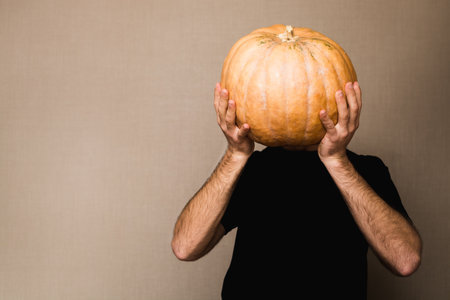 Young man in black t-shirt holding big pumpkin in front of his face.の写真素材