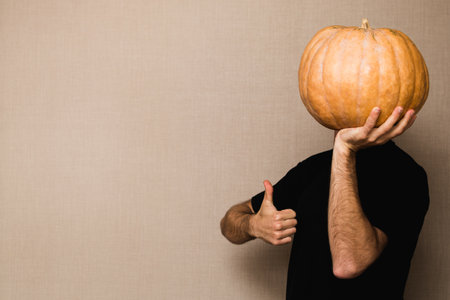 Young man in black t-shirt holding big pumpkin in front of his face, showing thumb up.の写真素材