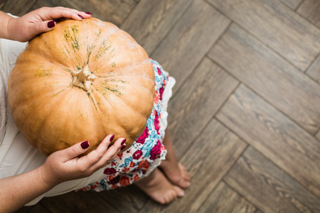 Young woman in white dress holding a big pumpkin on her lap.. Wooden floor background.の写真素材