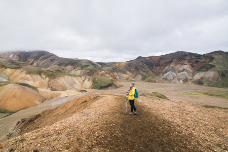 Woman in yellow raincoat hiking uphill in the colourful mountains in Landmannalaugar national park, Iceland.の写真素材