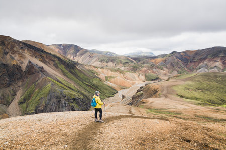 Woman in yellow raincoat hiking uphill in the colourful mountains in Landmannalaugar national park, Iceland.の写真素材