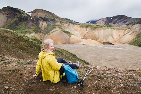 Woman in yellow raincoat overlooking the colorful mountains in Landmannalaugar national park, Icelandの写真素材