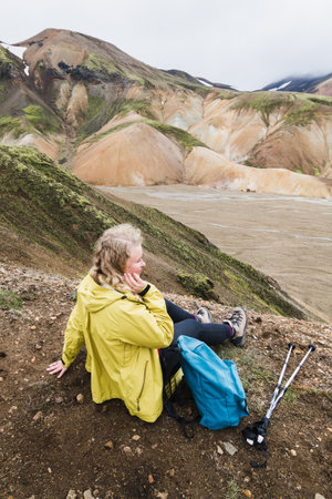 Woman in yellow raincoat overlooking the colourful mountains in Landmannalaugar national park, Iceland. Vertical orientation.の写真素材