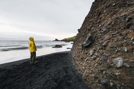 Young woman in a yellow raincoat standing on the black lava sand beach in Vik, Iceland.の写真素材