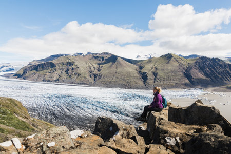 Woman sitting on rocks overlooking Skaftafellsjokull part of Vatnajokull glacier in Skaftafell national park, Iceland.の写真素材