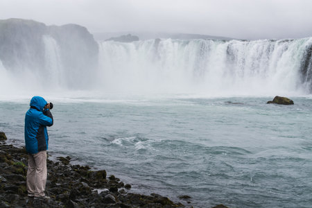 Photographer in blue jacket taking picture of Godafoss waterfall, Iceland.の写真素材