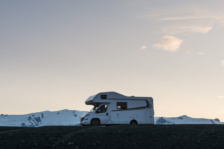 JOKULSARLON, ICELAND - AUGUST 2018: Campervan parked next to the black beach at sunset with snow...