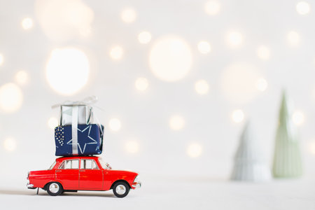 Red toy car with a christmas presents on the roof, garland bokeh on the background, shallow depth of field.の写真素材