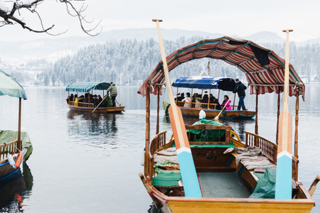 BLED, SLOVENIA - JANUARY 2015: boatmen transport tourists to the island on the lake. Empty boats on the foreground.のeditorial素材