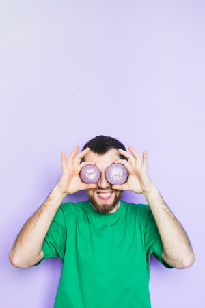 Young bearded man holding slices of red onion in front of his eyes, mouth wide open. Light green background, vertical orientation, copy space.の写真素材