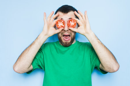 Young bearded man holding slices of red tomatoes in front of his eyes, mouth wide open. Light purple background, copy space.の写真素材