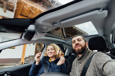 Young couple taking selfie in a car with glass roof. Wide angle lens shot. Bearded man and blonde woman smiling.の写真素材