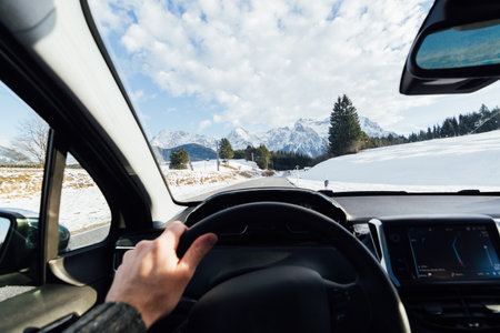 View from car driver's seat over winter Alpine road heading to mountains in Austriaの写真素材