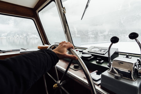 HALLSTATT, AUSTRIA - JANUARY 2019: view over Hallstatt town and Alps mountains from ferry boat captain's cabin. Hand on the steering wheel.のeditorial素材