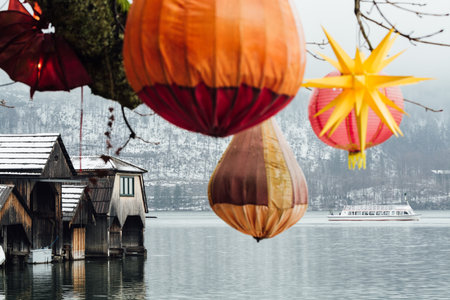 HALLSTATT, AUSTRIA - JANUARY 2019: lake ferry passing the wooden boat houses of Hallstatt old town. Christmas lights on the foreground.のeditorial素材