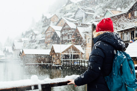 Woman in red hat enjoying the view over lakefront Hallstatt old town during snow storm, Austria.の写真素材